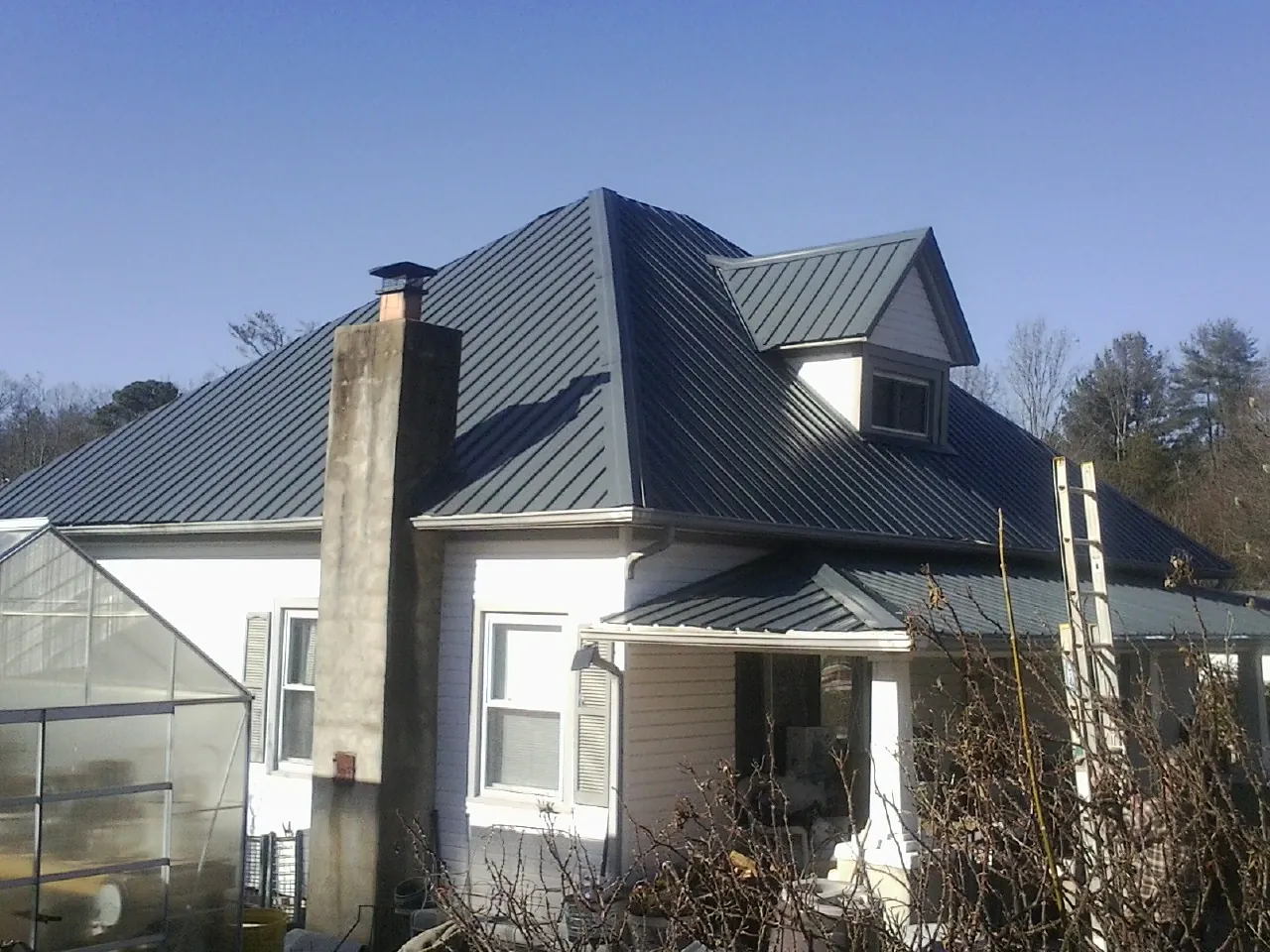 Dark blue standing seam metal roof on a white farmhouse with dormer — Slate & Tile Roof Repair by Roofing Brothers in Seagrove