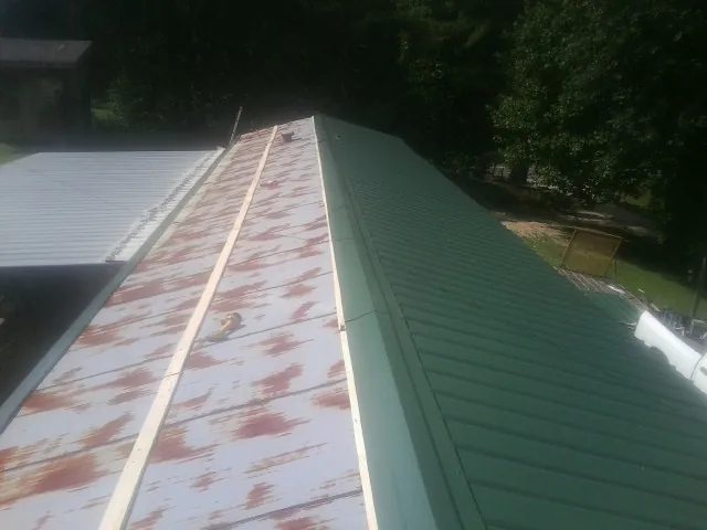 Old rusted panels beside newly installed green metal roofing — Wind Damage Roof Repair by Roofing Brothers in Seagrove