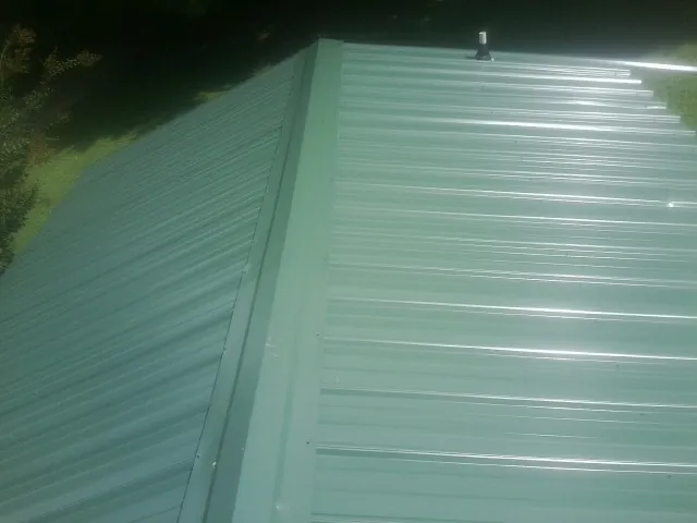 New green metal panels meeting at the ridge of a roof — Flat Roof Repair work by our crew in Seagrove