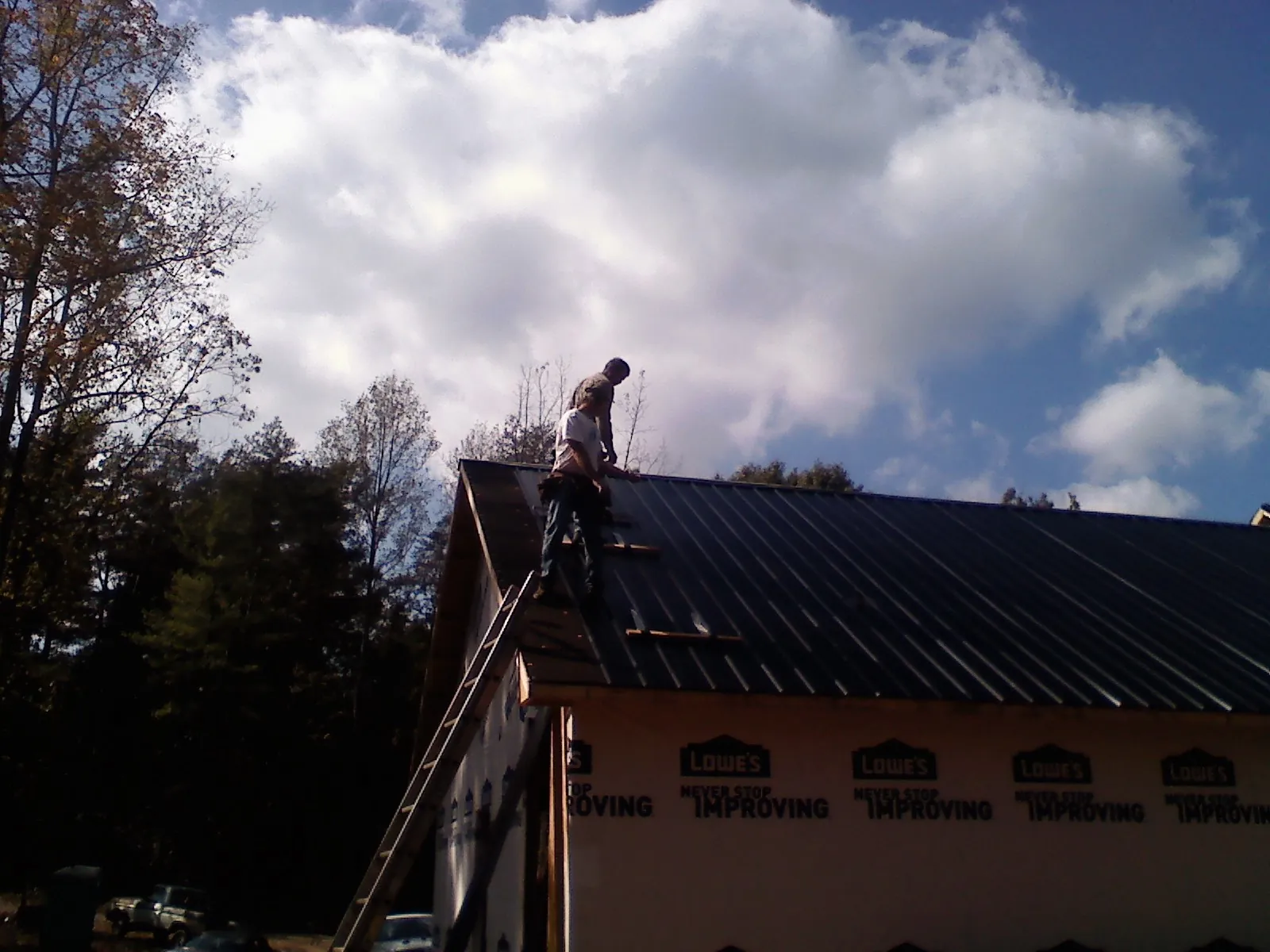 Roofer fastening dark metal panels high against a cloudy sky, from a Roof Inspection job in Seagrove