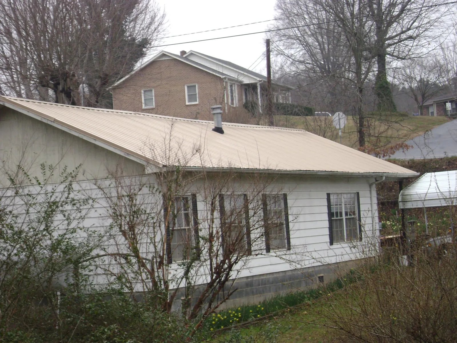 Tan metal roof on a white sided house set into a hillside — Commercial Roofing by Roofing Brothers in Seagrove