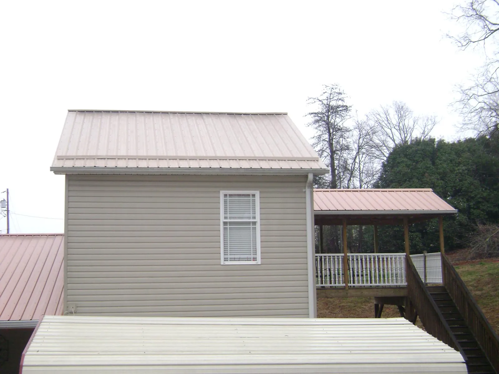 Tan metal roofs on a two story addition and attached porch, from a Roof Replacement job in Seagrove